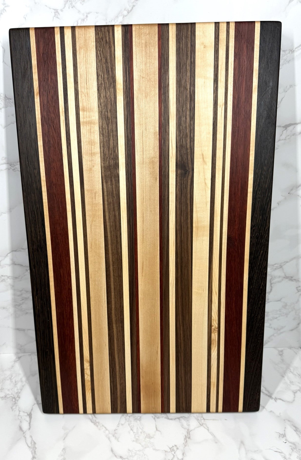 "The OKI 25 – handcrafted cutting board made from Wenge, Black Walnut, Padauk, and Maple."
